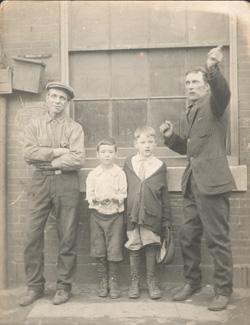 John Frank Keith, Two men and two boys in front of factory window, gelatin silver print on postcard mount, Philadelphia: ca. 1917.